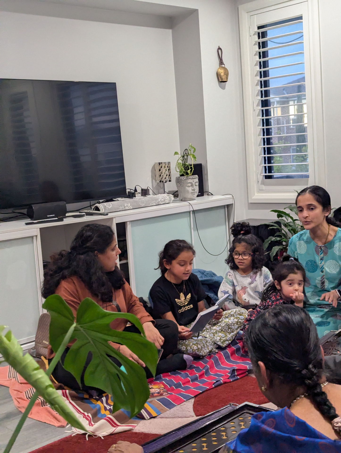 Children and mothers gathered around the bhajan book at practice