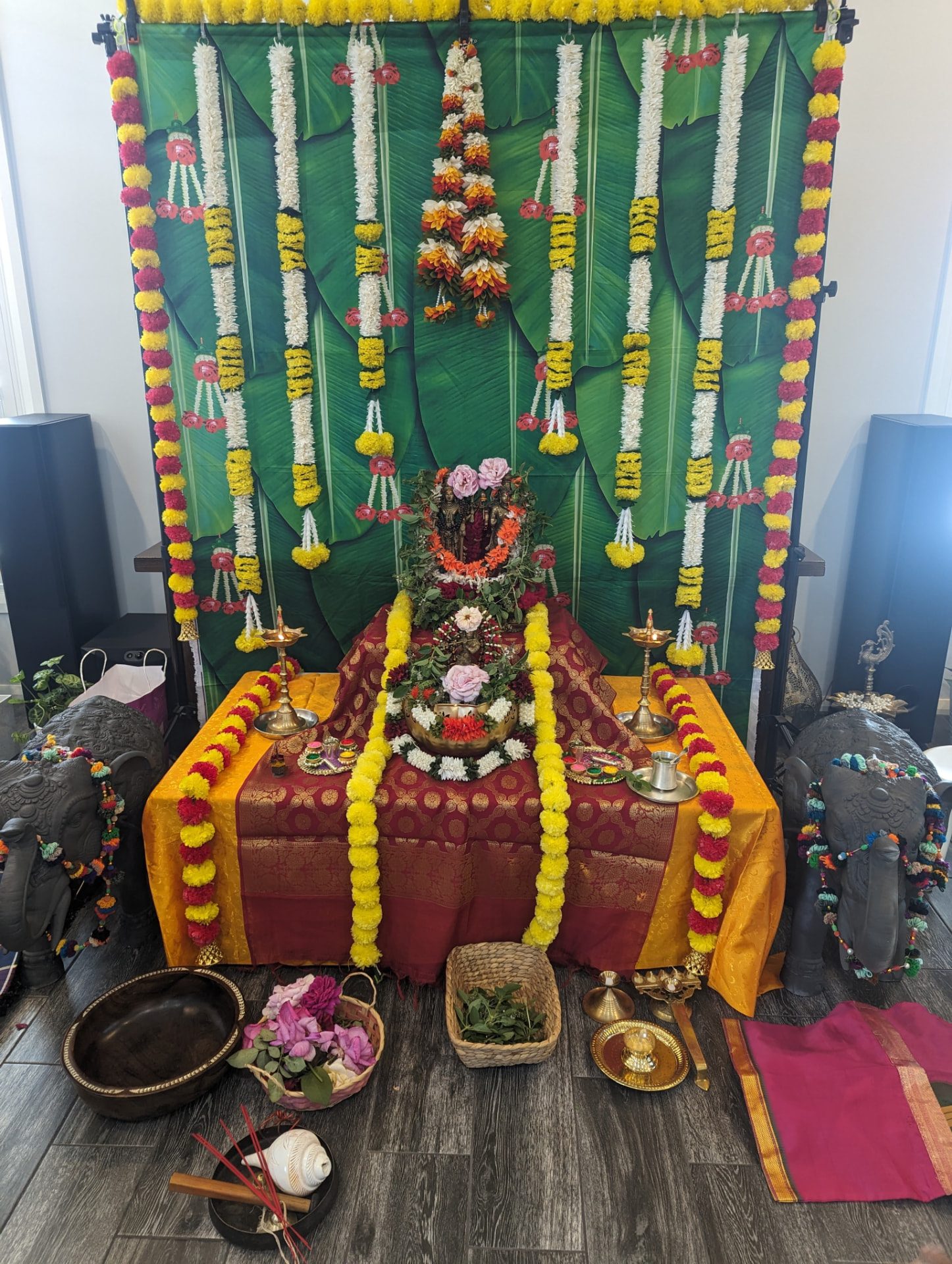 The Holi altar — banana-leaf backdrop, marigold and jasmine garlands, and lamps lit for puja
